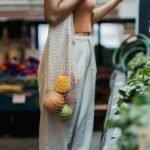 A shopper carrying reusable bags filled with eco-friendly products, symbolizing the environmental impact and sustainability of consumerism.